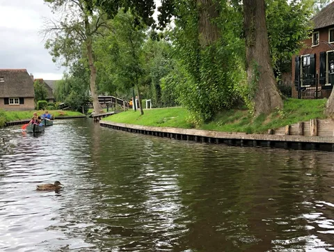 Barco de alquiler sin conductor pasando bajo un puente de madera en arco en Giethoorn